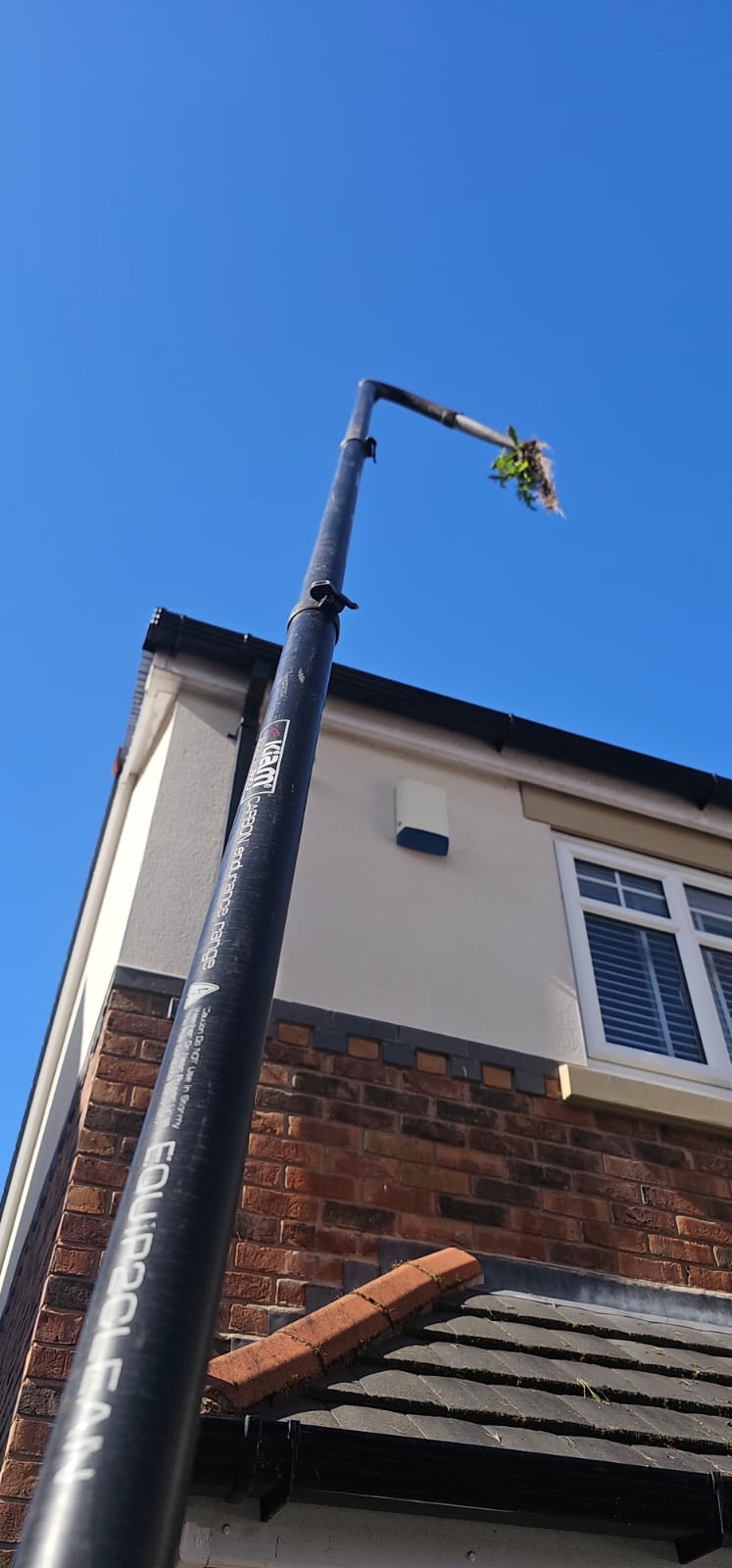 Gutter vacuum pole removing vegetation from a Wirral roof edge