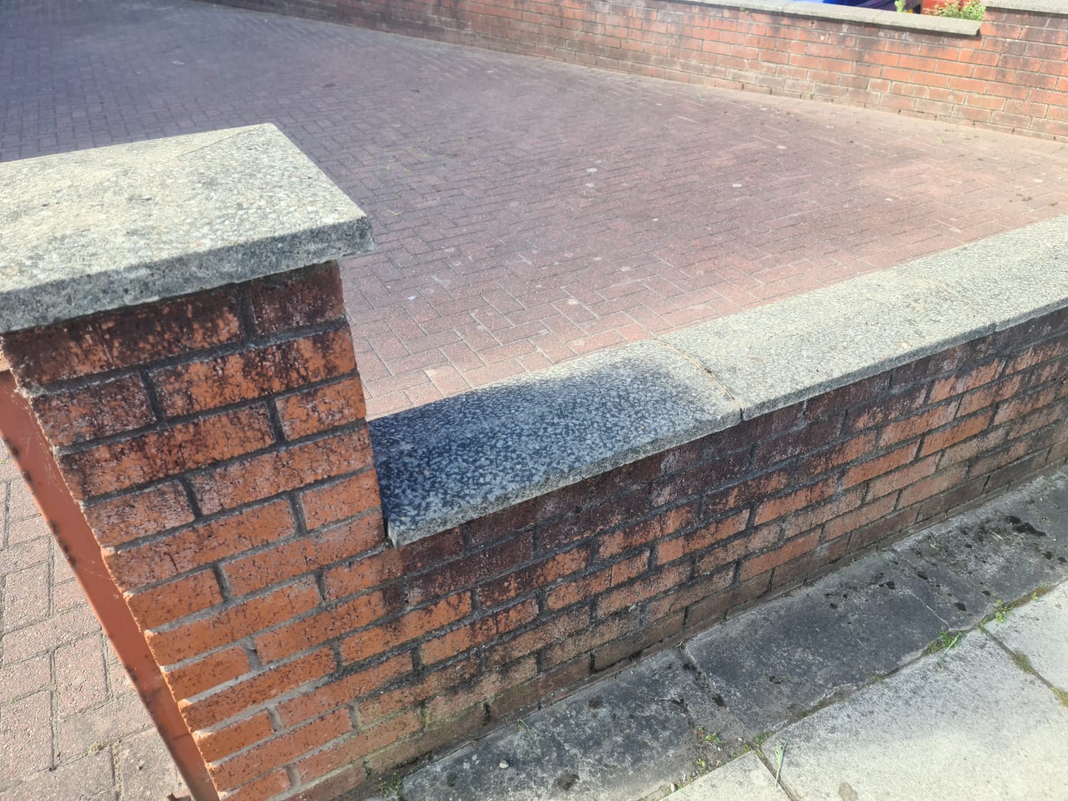 Stained paving beside a brick wall before jet washing in the Wirral