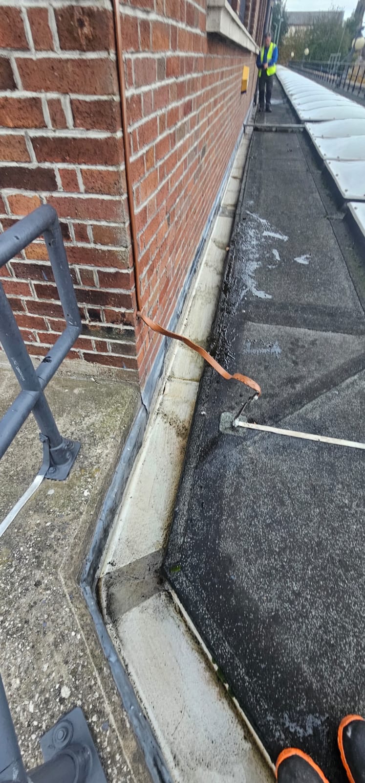 Narrow roof gutter being cleared beside brickwork in the Wirral
